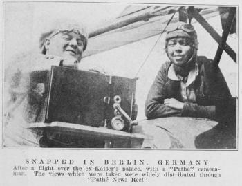 Black and white photo of Bessie Coleman leaning over the side of her plane talking to a cameraman.